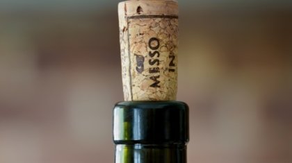 Bottiglia di vino aperta con tappo di sughero accanto a un bicchiere di vino rosso