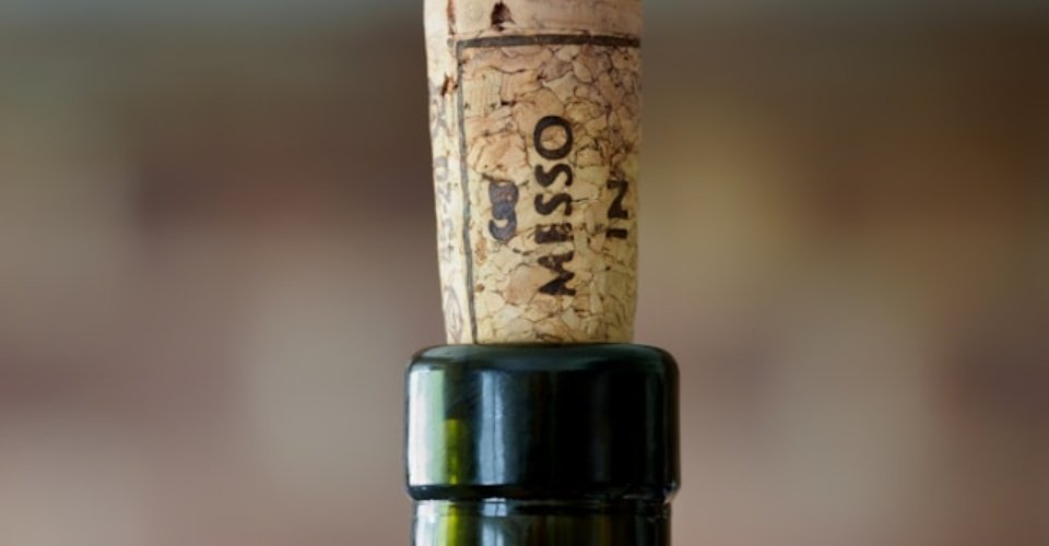 Bottiglia di vino aperta con tappo di sughero accanto a un bicchiere di vino rosso