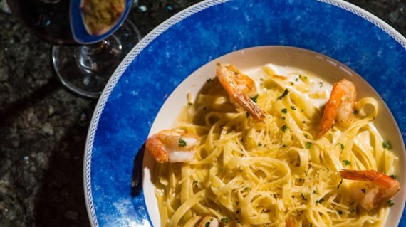 Piatto di pasta con pesce e bicchiere di vino rosso su tavola