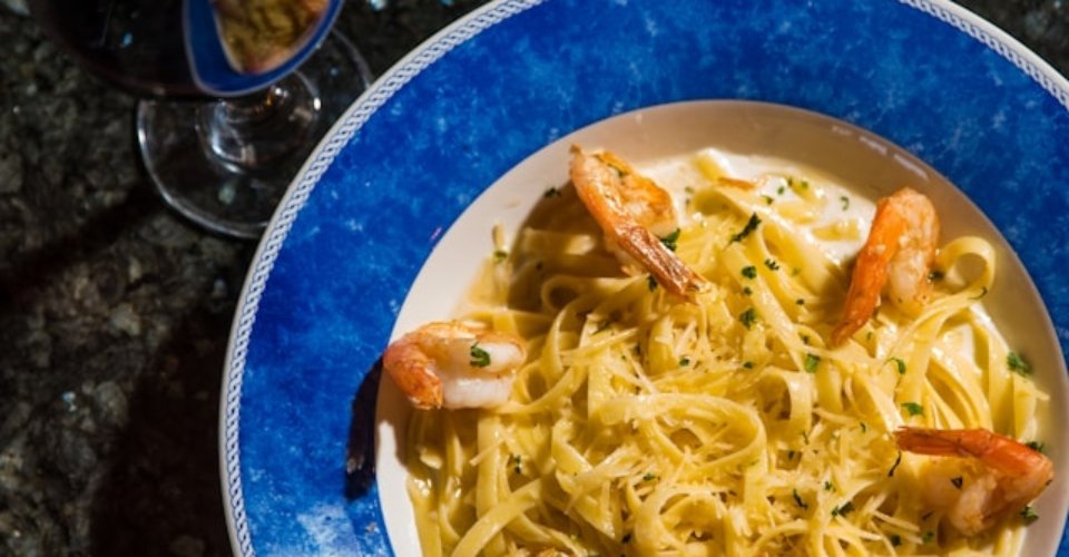 Piatto di pasta con pesce e bicchiere di vino rosso su tavola