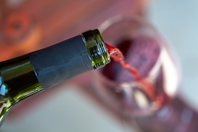 Mano che versa lentamente vino rosso in un calice di vetro